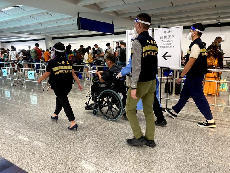 照片顯示,受害人是一名中年男人,抵達香港國際機場時坐著輪椅,由身穿防護衣的職員及入境處人員護送。(香港政府新聞處)